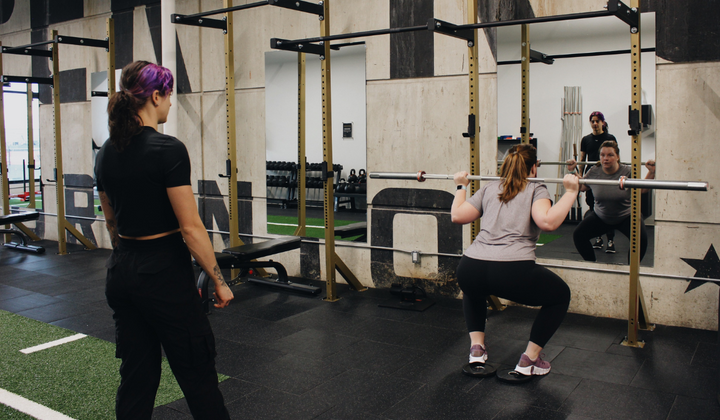 Coach Chelsie watches Jen perform a barbell back squat warm up set